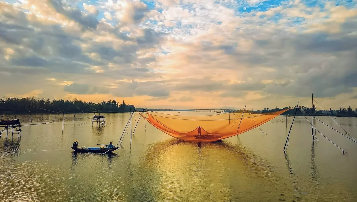 A giant fishing net glows orange under a golden sunset sky on a river near Hoi An.