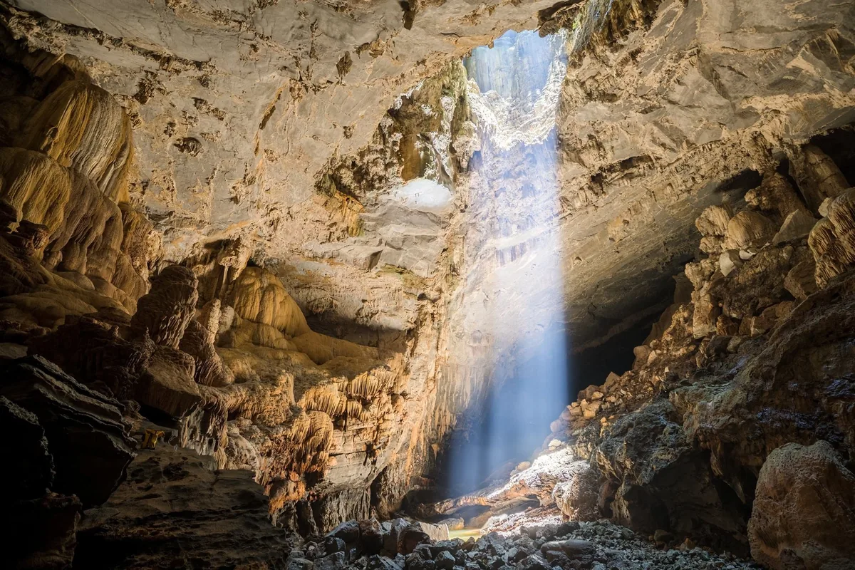 A shaft of sunlight pierces through a ceiling opening into the vast limestone chamber of Paradise Cave.