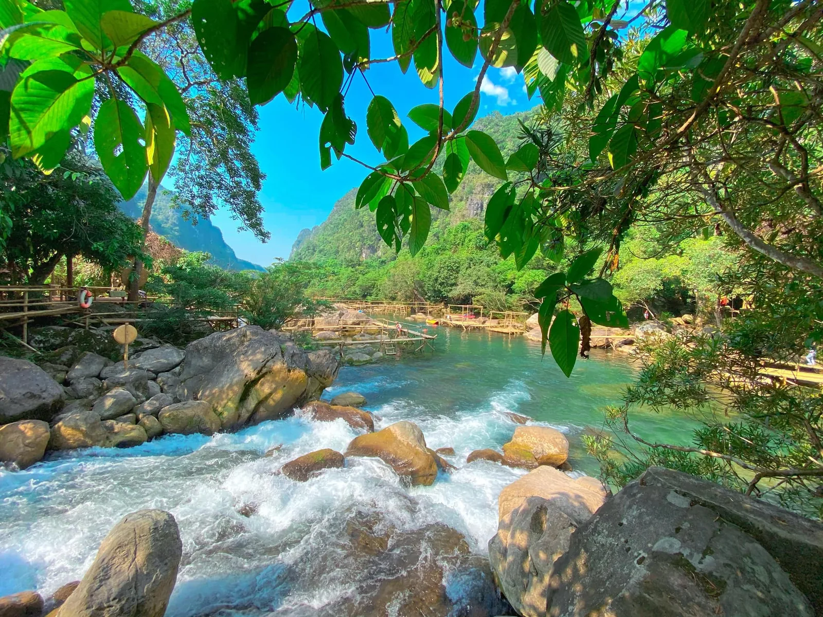 Turquoise river cascades over boulders through a lush green valley at Suoi Moc, Phong Nha.