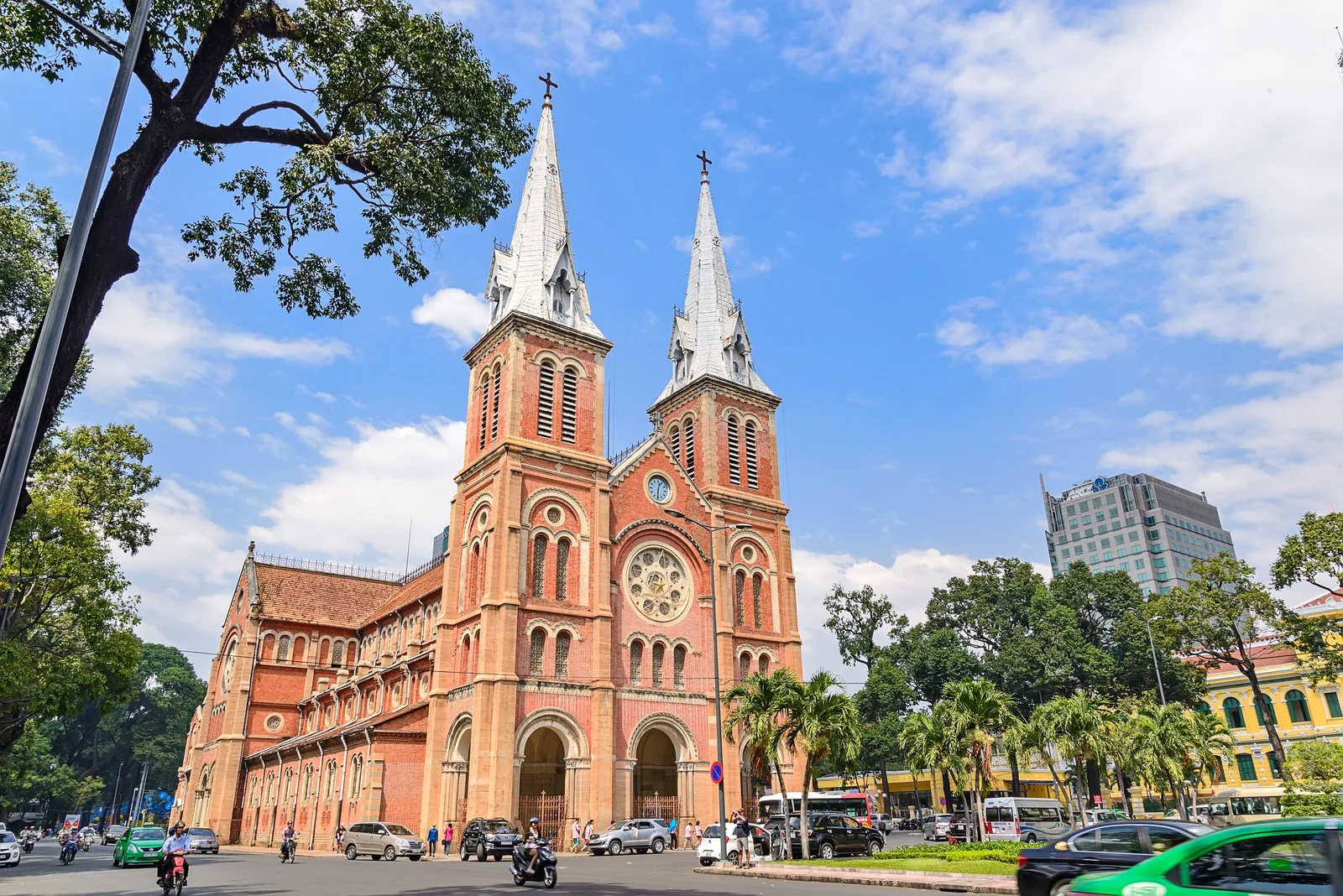 Twin bell towers of Notre-Dame Cathedral rise over a busy street in Saigon under a bright blue sky.