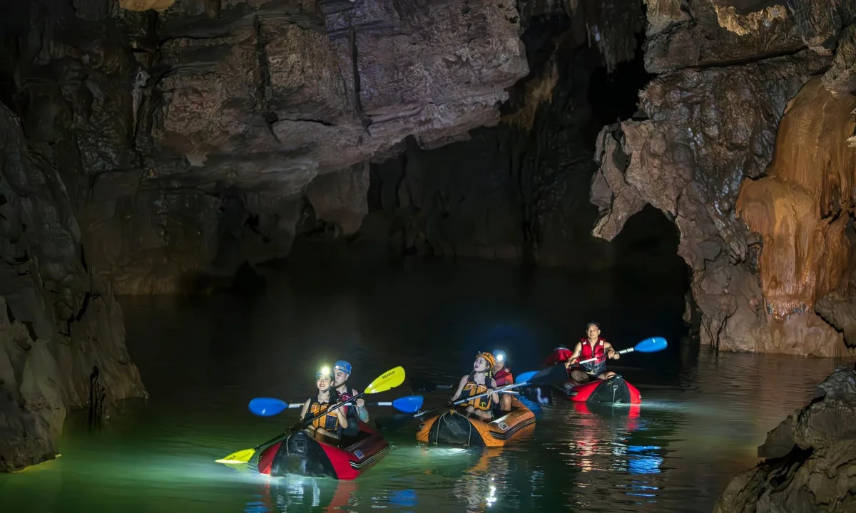 Kayakers with headlamps paddle through the dark waters of Phong Nha Cave, surrounded by towering limestone formations.