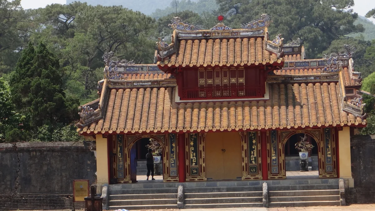 A traditional tiled-roof gate building with red and gold accents at the Minh Mang Tomb in Hue.