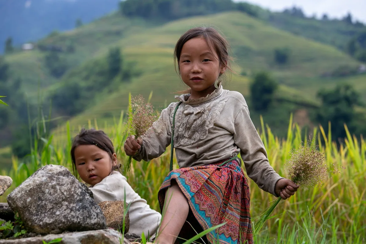 Two young children in traditional dress play among rice terraces in the hills near Sapa.