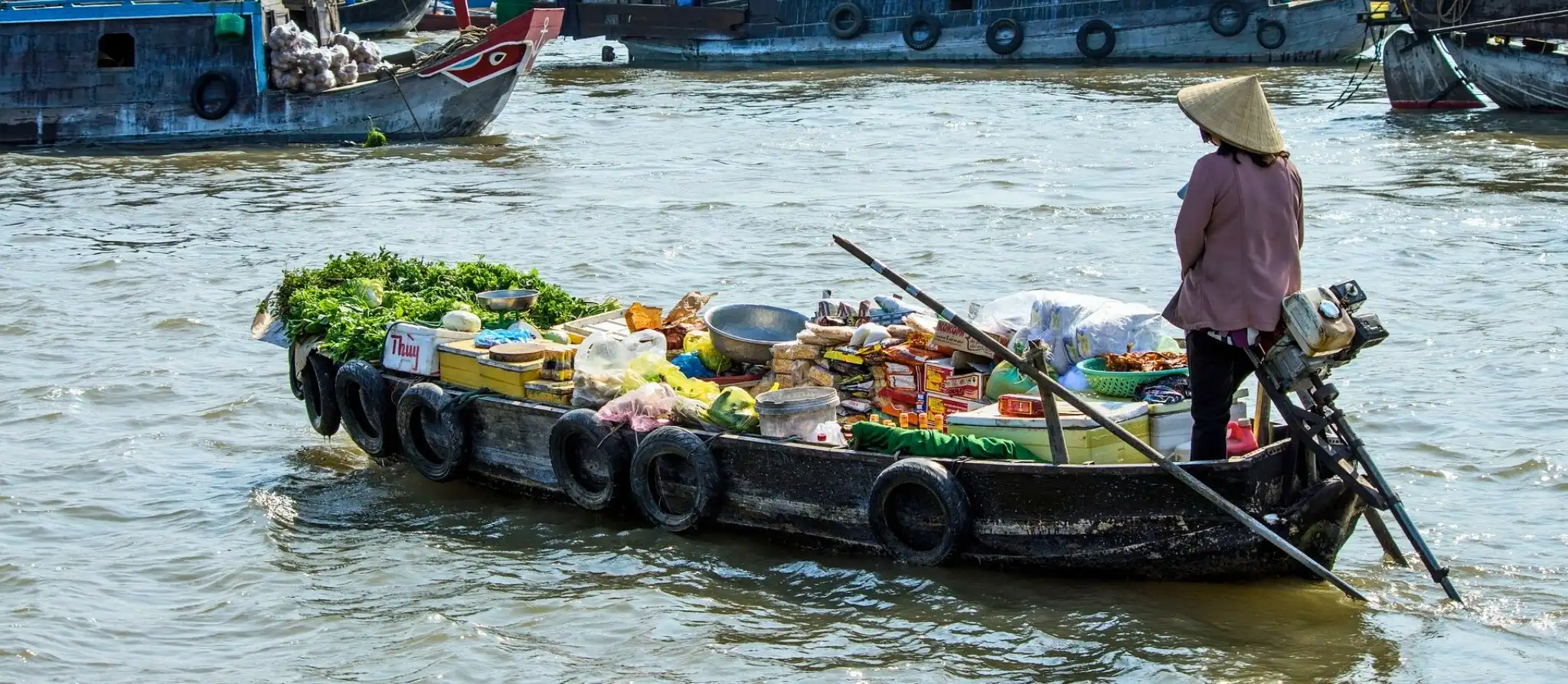Trader passing produce between boats at Cai Rang floating market