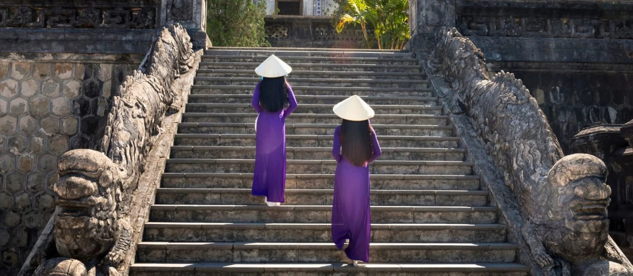 Woman in a conical hat walking past an old wall in Hue